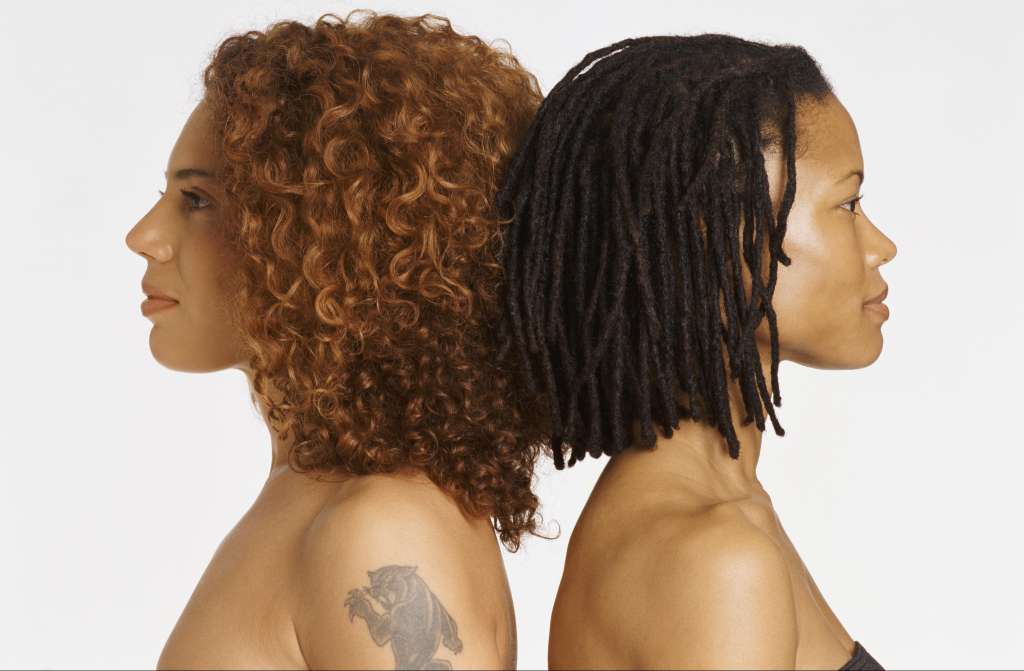 Studio Portrait of Two Young Women Back to Back, One With a Tattoo