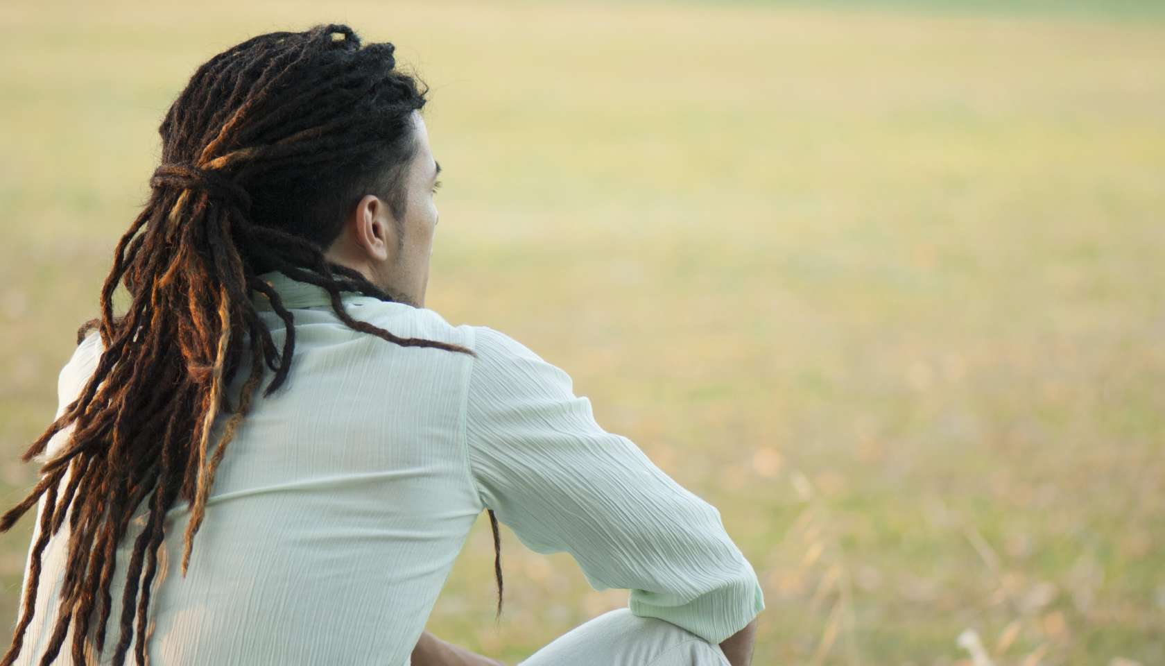 Man with dreadlocks sitting outdoors, rear view